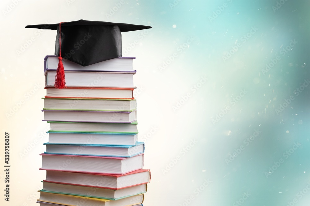 Stack school books with black graduation hat