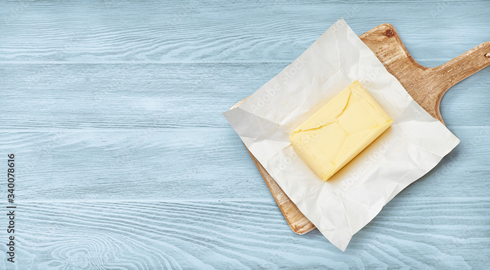 包装纸和木板上的一块黄油。蓝色木质背景上的黄油俯视图。