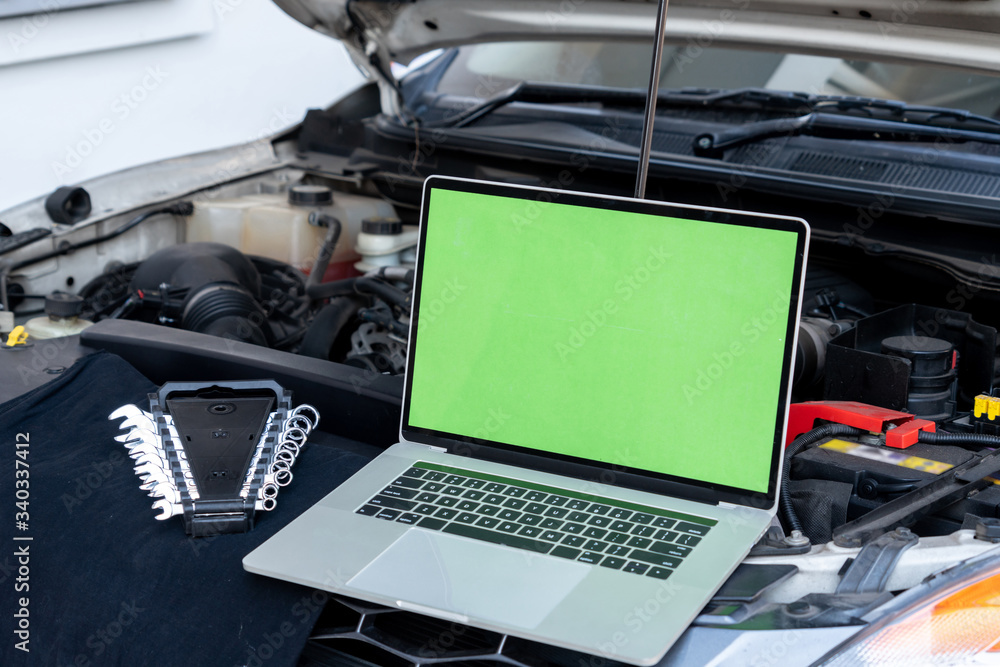 汽车引擎盖上的笔记本电脑用于发动机诊断。汽车修理厂维修服务理念。