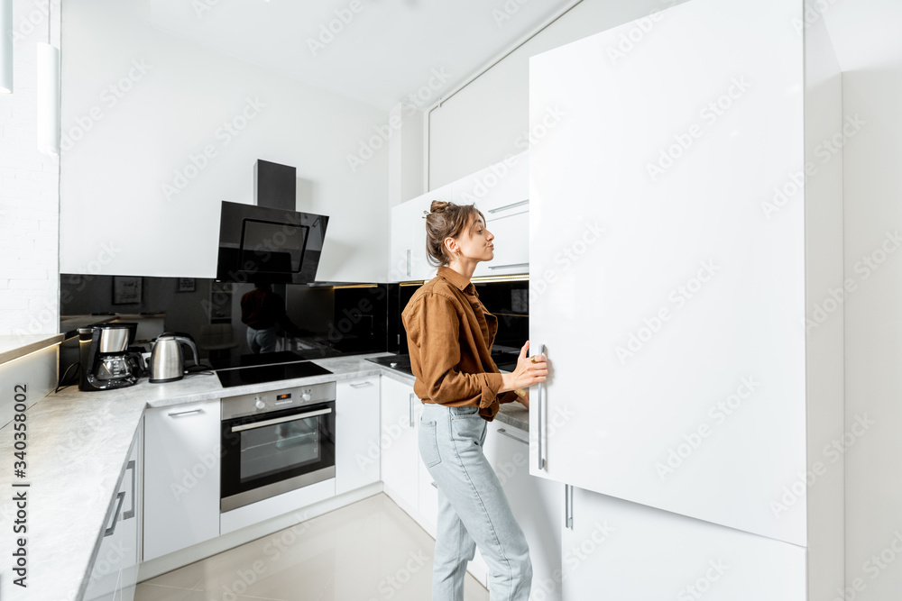女人看着冰箱，站在家里的现代厨房上