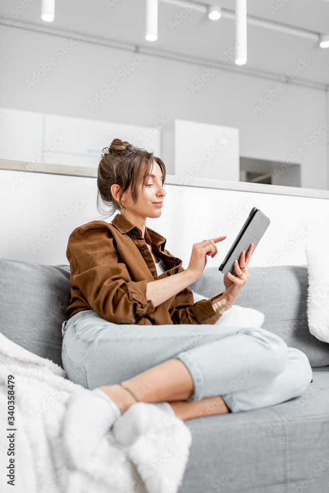 年轻放松的女性坐在沙发上用数字平板电脑工作或上网a