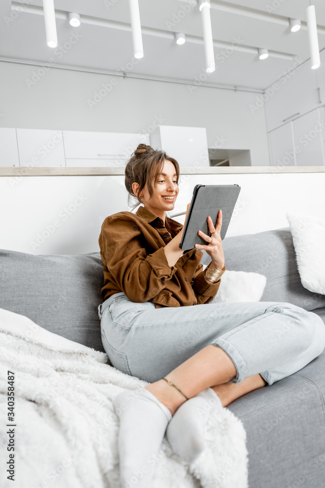 年轻放松的女性坐在沙发上用数字平板电脑工作或上网a