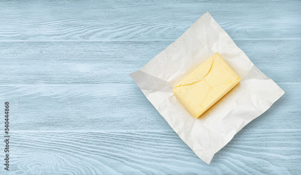 蓝色木质背景上隔离的包装纸上的一块黄油。黄油俯视图。