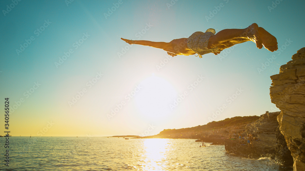 特写：一名运动员在日落时从悬崖上跳下，头朝下坠入大海