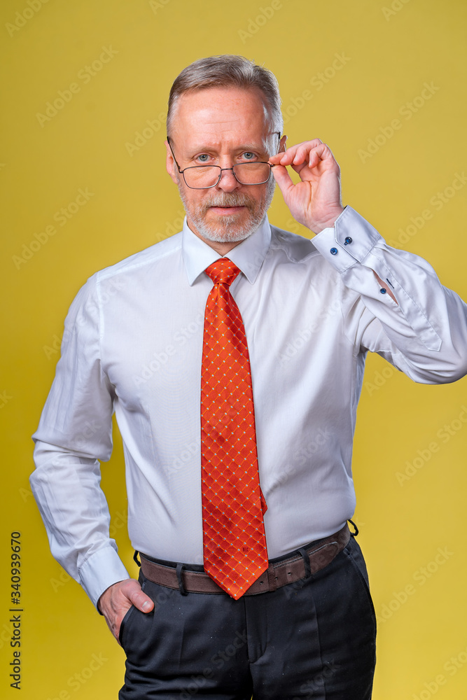 Portrait of a senior man in glasses. Man looking at camera. Business man in studio, yellow backgroun