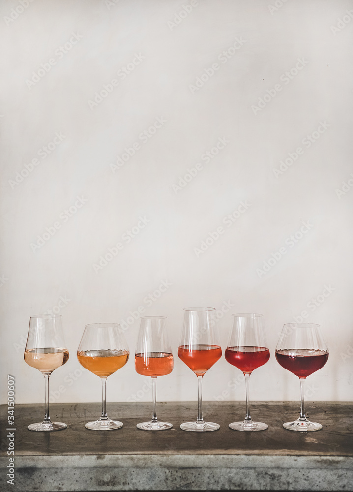 Various shades of Rose wine in stemmed glasses placed in line from light to dark colour, white wall 