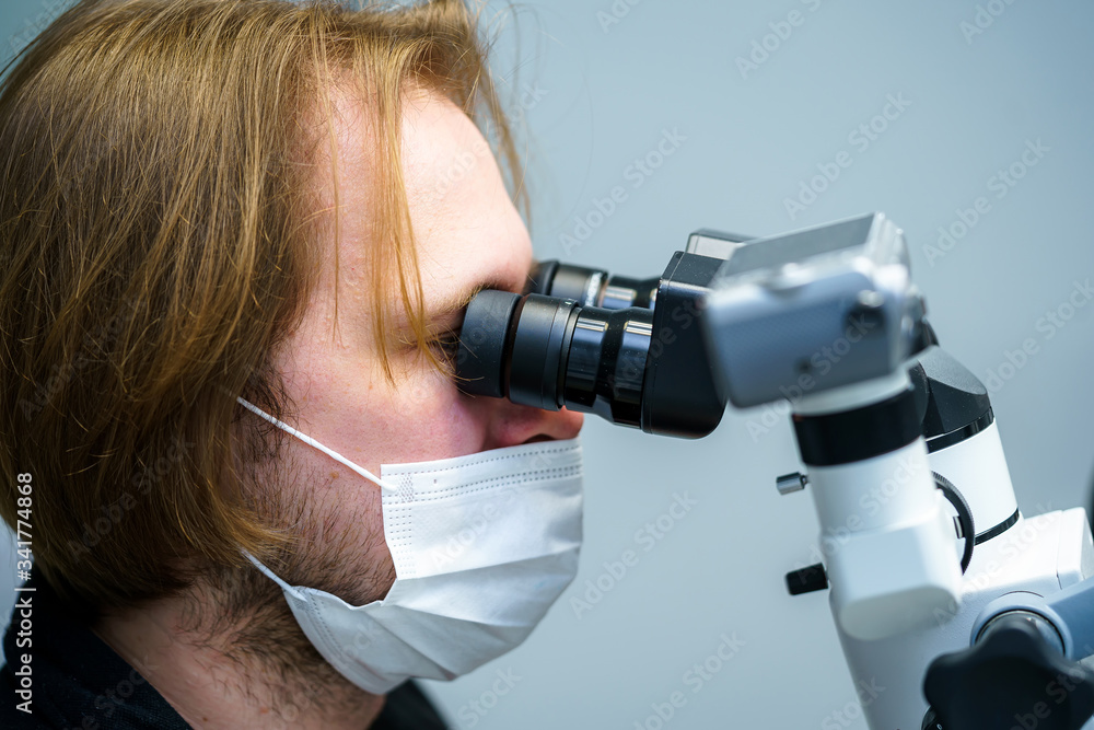 Dentist with protective mask and gloves repair tooth of a client at modern ambulant with microscope.