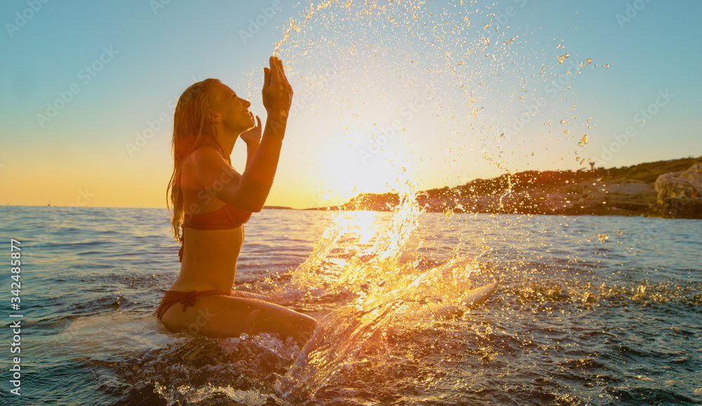 特写：微笑的冲浪女孩坐在冲浪板上泼水