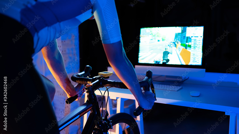 Asian man cycling on the machine trainer he is exercising in the home at night.he play online bike g