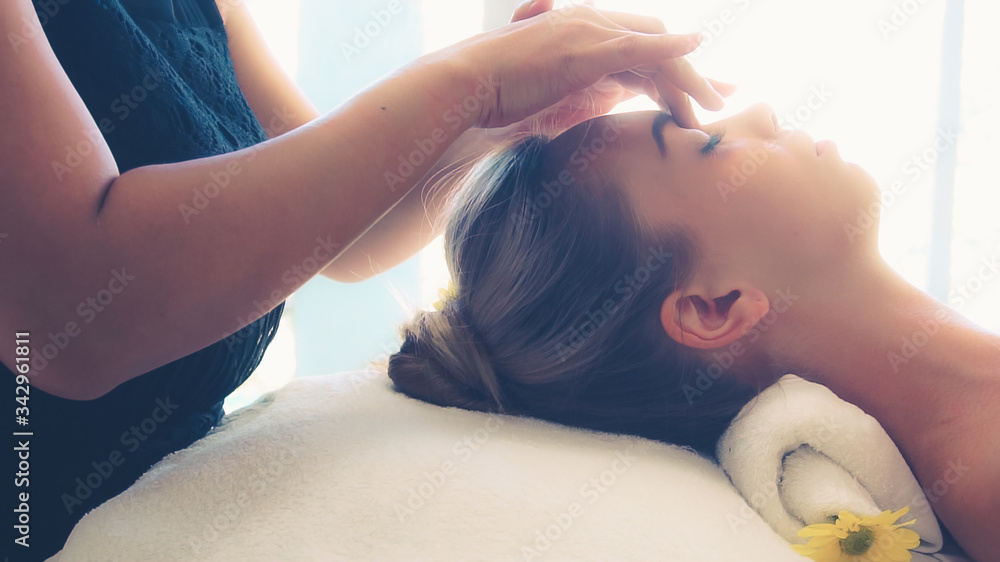 放松的女人躺在水疗床上，接受按摩治疗师的面部和头部按摩水疗
