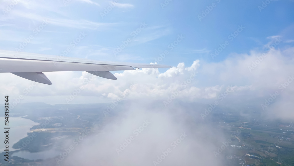 wing of airplane flying through clouds over receding land with towns rivers mountains against sky wi