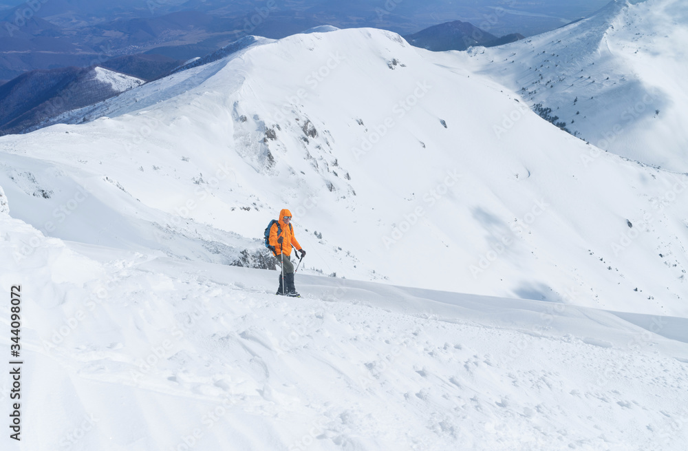 高山登山者穿着亮橙色软壳夹克，使用登山杖攀登雪地