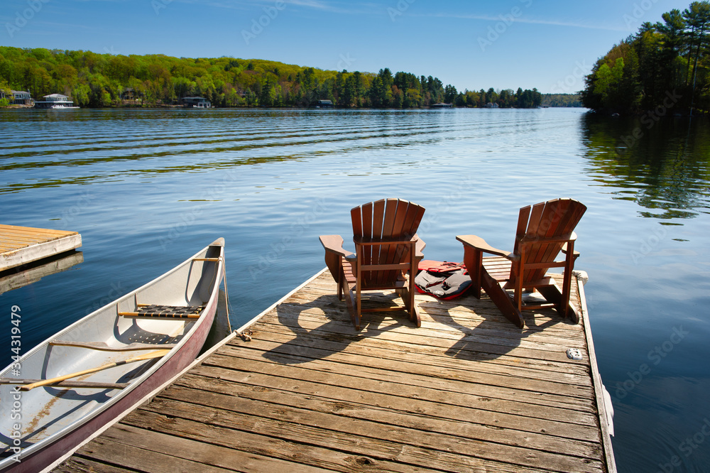 两把阿迪朗达克椅子放在一个木制码头上，面向加拿大安大略省马斯科卡市的蓝色湖水。a
