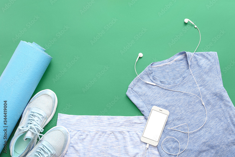 Sportswear, yoga mat and mobile phone on color background