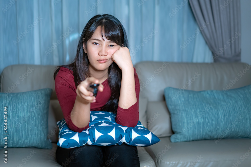 Young asian woman watching television suspense movie or news looking very drowsy or bored late night