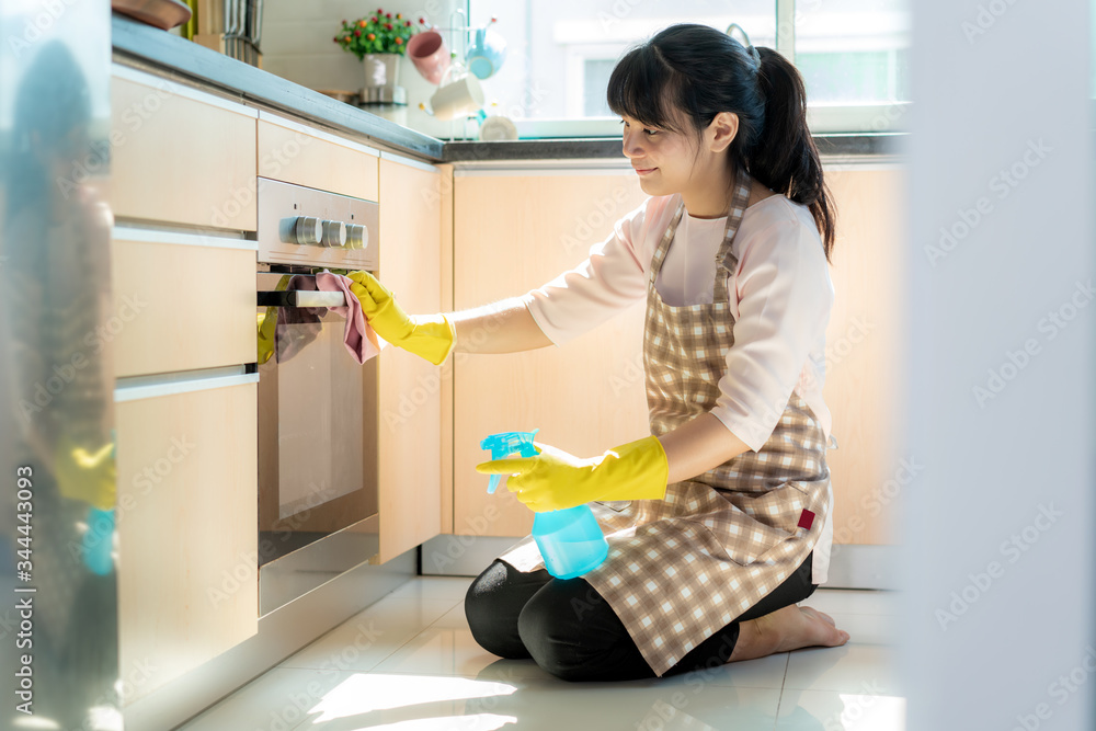 Asian woman wearing rubber protective gloves cleaning oven in her home during Staying at home using 