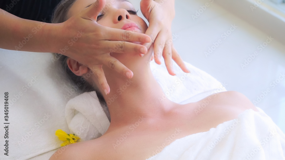 放松的女人躺在水疗床上，接受按摩治疗师的面部和头部按摩水疗治疗