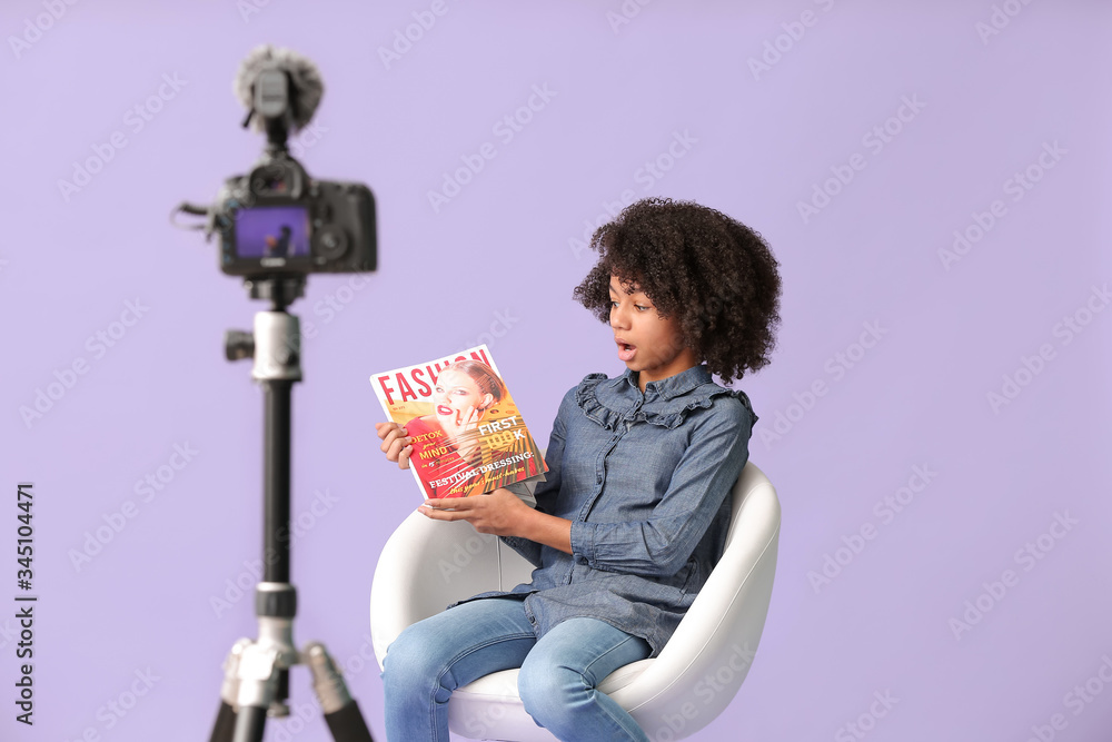 African-American teenage fashion blogger recording video on color background