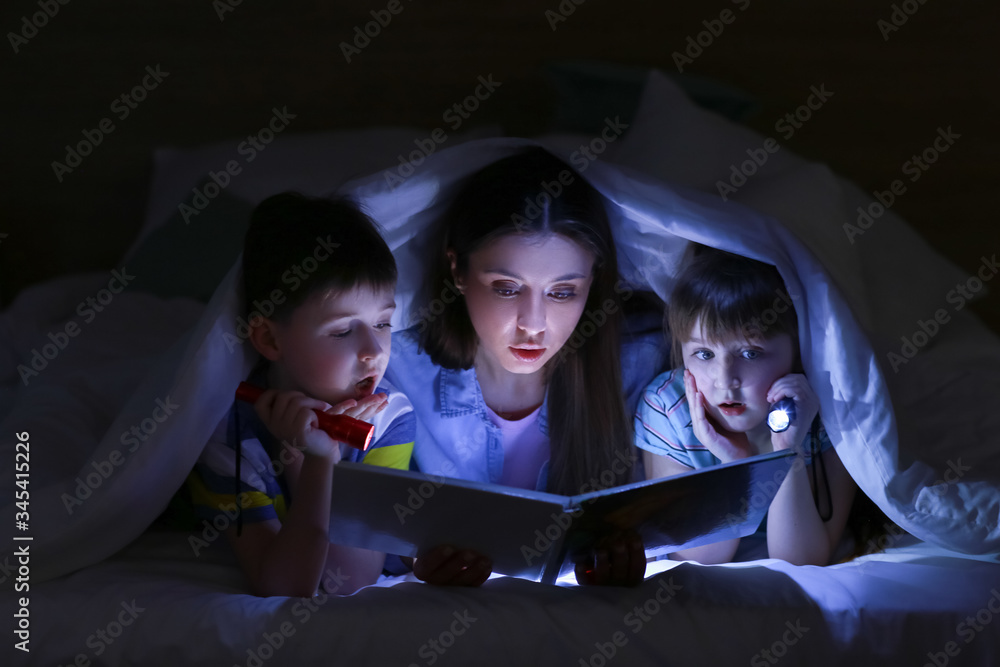 妇女和她的小孩晚上在毯子下看书