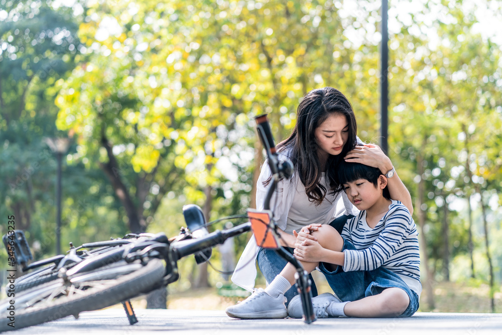 Asian young mother encourage son to ride bicycle in park. Mother sit beside kit, hold son hand and h