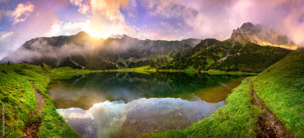在阿尔卑斯山的一个湖泊上，壮丽的日出，群山、彩云和薄雾反射