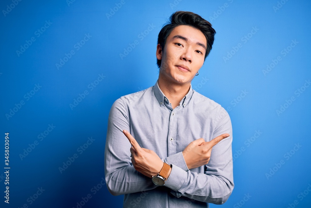 Young handsome chinese man wearing casual shirt standing over isolated blue background Pointing to b