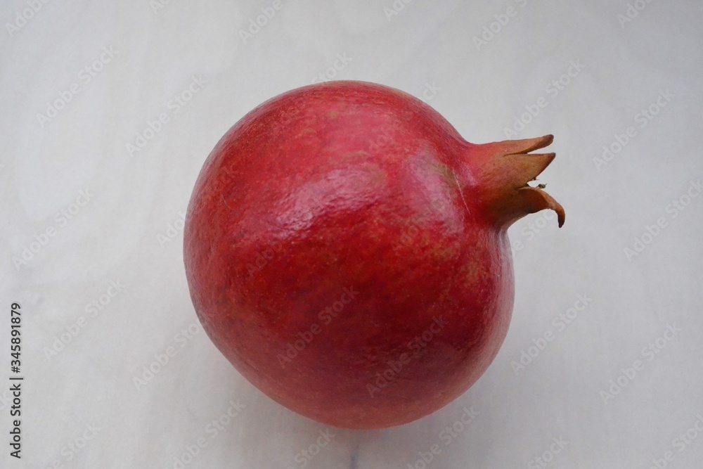 一个成熟的红色大石榴的图像，由茎向右翻转，在木质纹理（松树）上