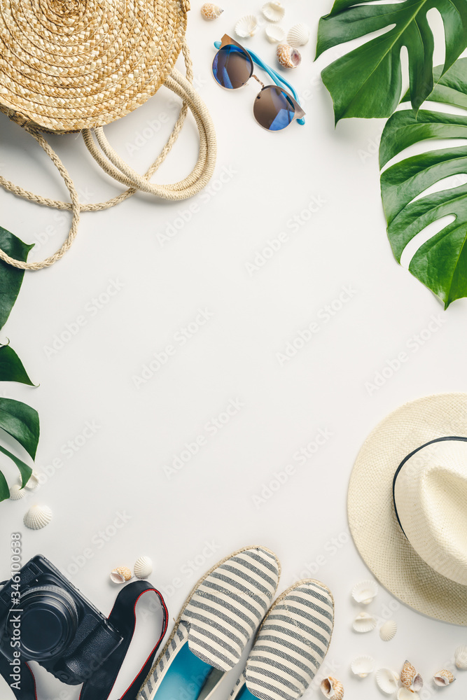 白色背景下的草帽、相机、包、夏鞋、太阳镜、贝壳和热带树叶，