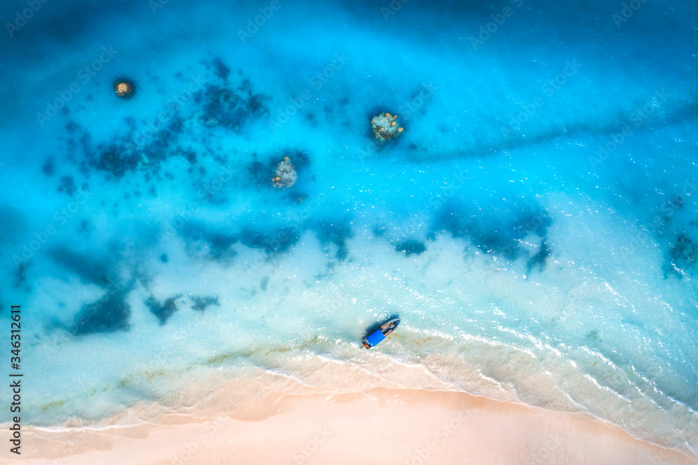 Aerial view of alone fishing boat in blue transparent water at sunset in summer. Top view of boat, y