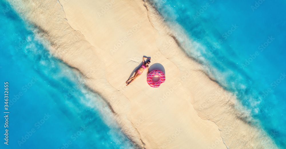 Aerial view of beautiful young lying woman with pink donut swim ring on the white sandy beach and se