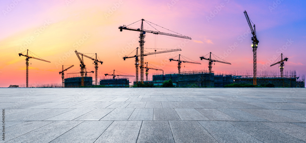 Empty square floor and construction site silhouette at sunrise.