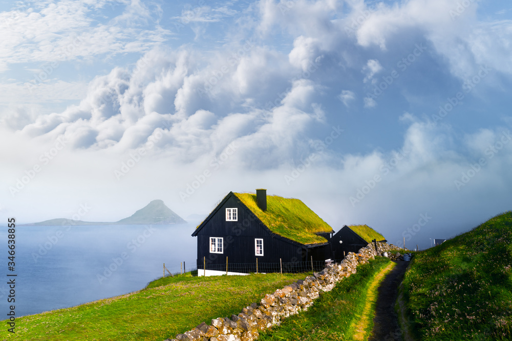 在Velbastadu，一栋典型的草坪顶草屋顶和蓝色多云天空的房子的雾蒙蒙的晨景