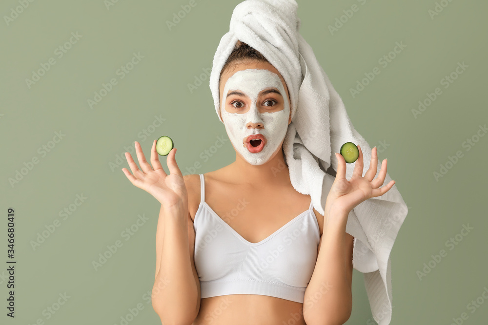 Beautiful young African-American woman with cucumber slices and facial mask on color background