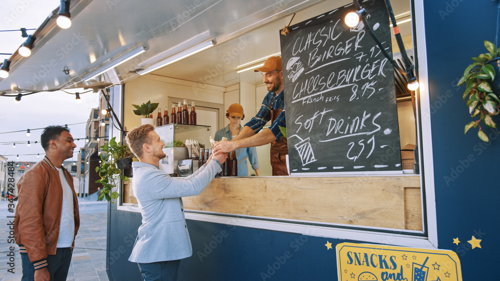 Food Truck Employee Hands Out a Freshly Made Gourmet Burger to a Happy Young Man in a Suit. Street F