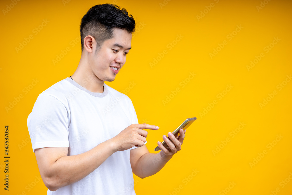 黄色背景下，一个亚洲年轻人孤立地看着手机。