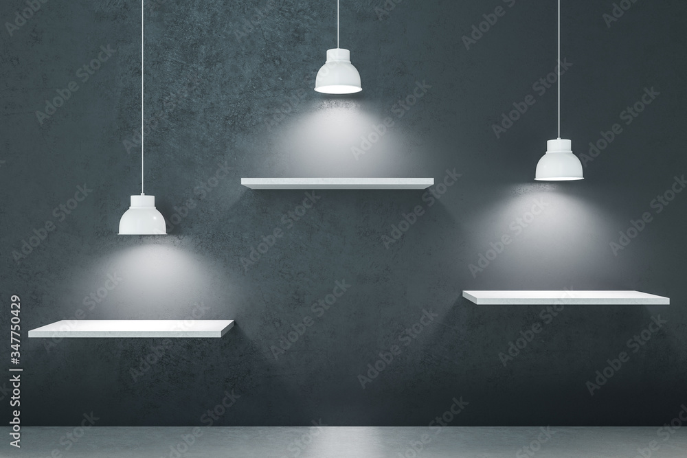 Three white shelf on gray concrete wall with lamps.