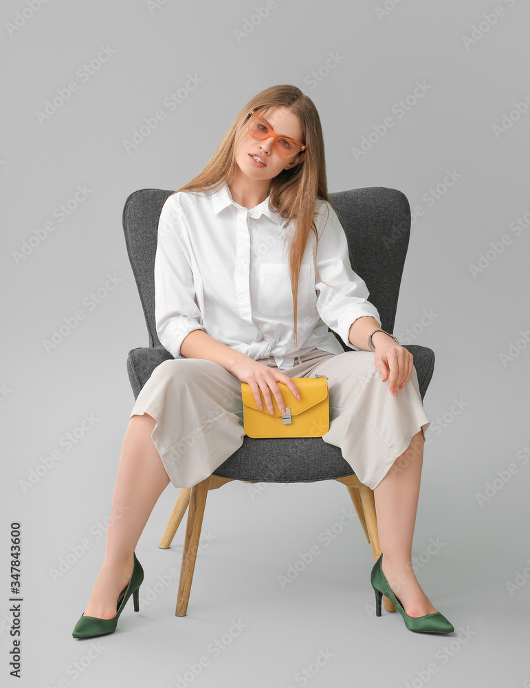 灰色背景下，坐在扶手椅上，带着时尚包包的美女