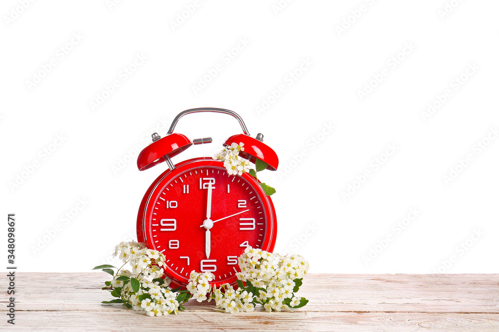 白色背景下的闹钟和桌子上的花。春天的时间