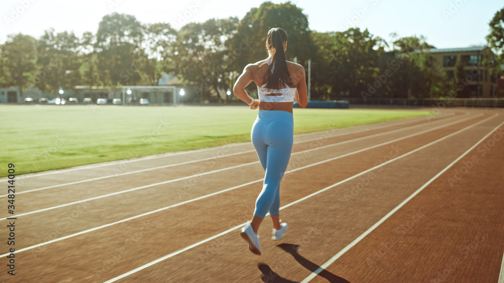 穿着浅蓝色运动上衣和紧身裤在体育场慢跑的美丽健身女孩。她是跑步者