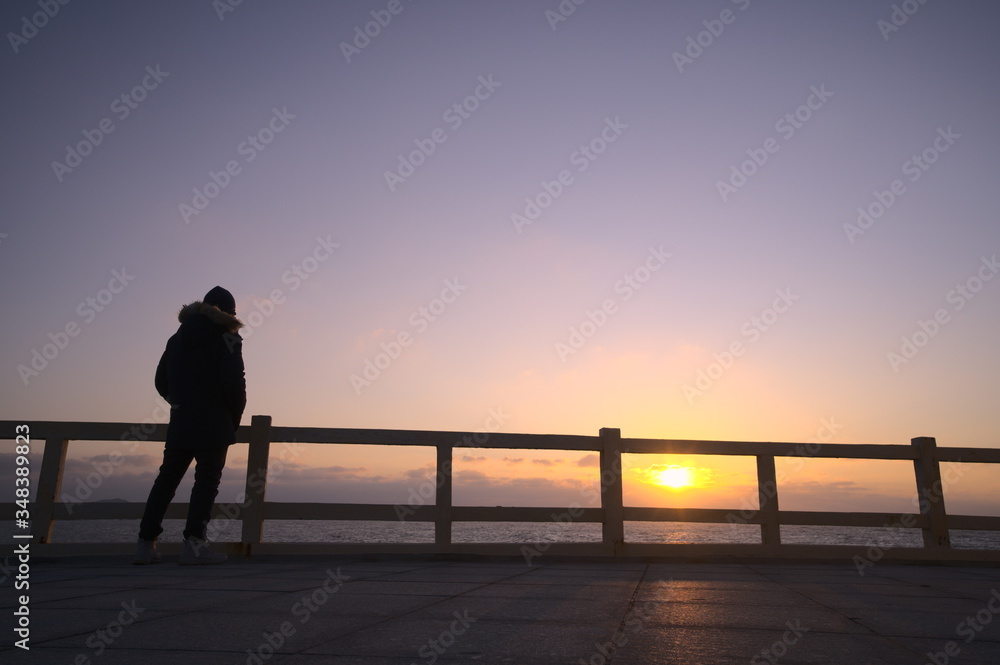 悲伤的男人站在海边围栏前的剪影，低角度视角，日落背景，复制空间