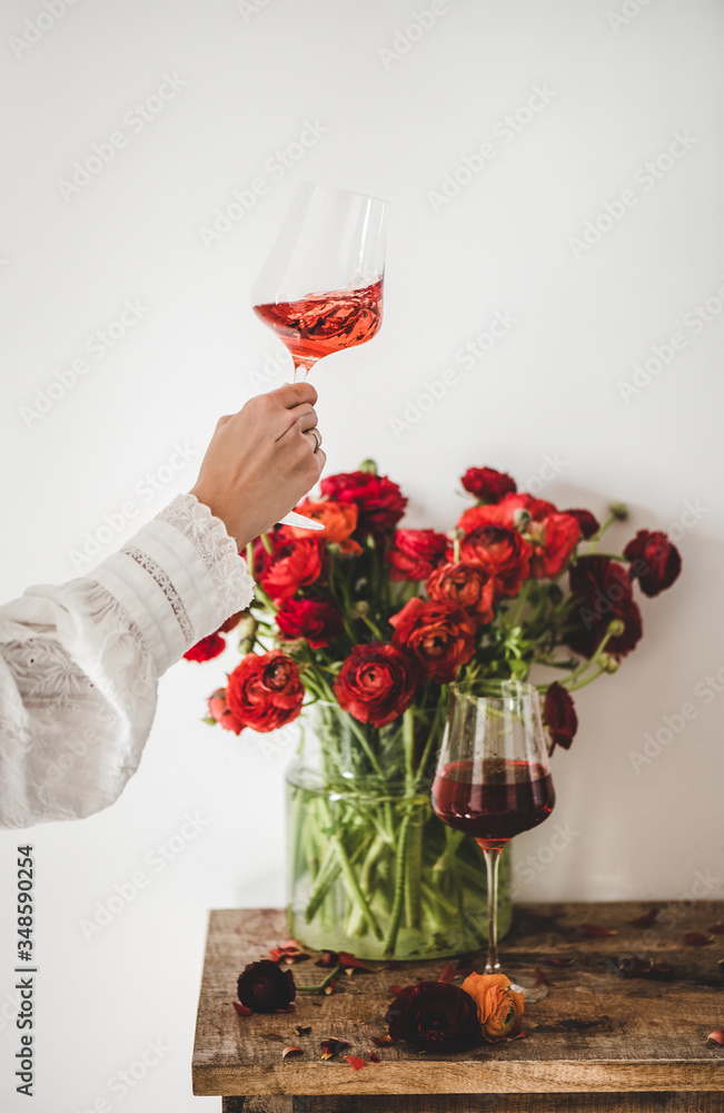 女人手拿酒杯里的玫瑰酒和乡村木桌上的红色春花花束