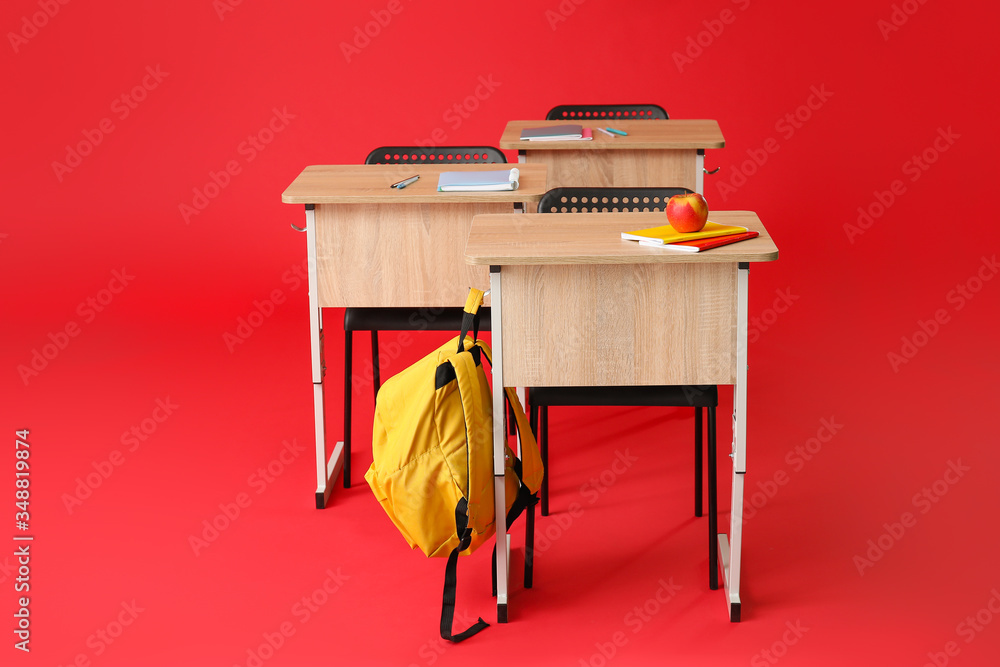 School desks with chairs and backpack on color background