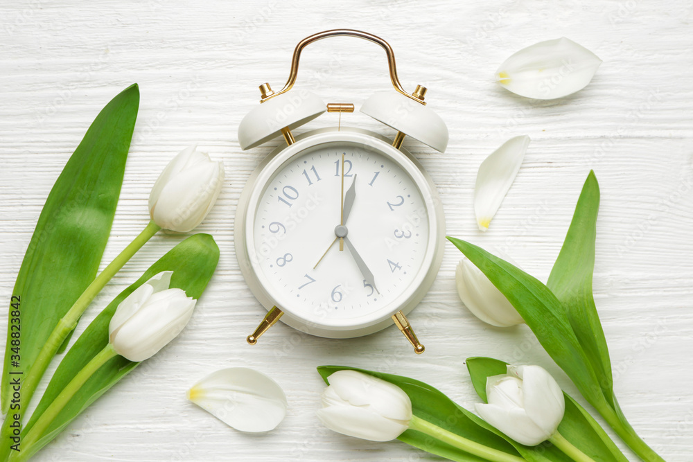白色木质背景上的闹钟和花朵。春天的时间
