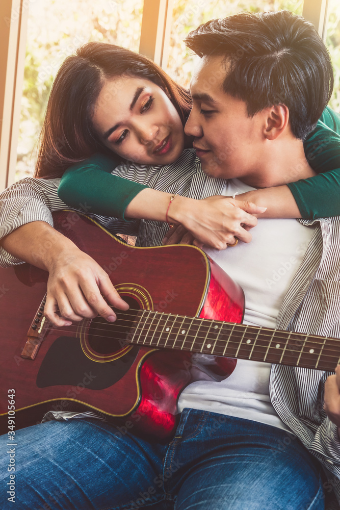 年轻的亚洲情侣在家的客厅里一起弹吉他唱歌。音乐与生活方式c