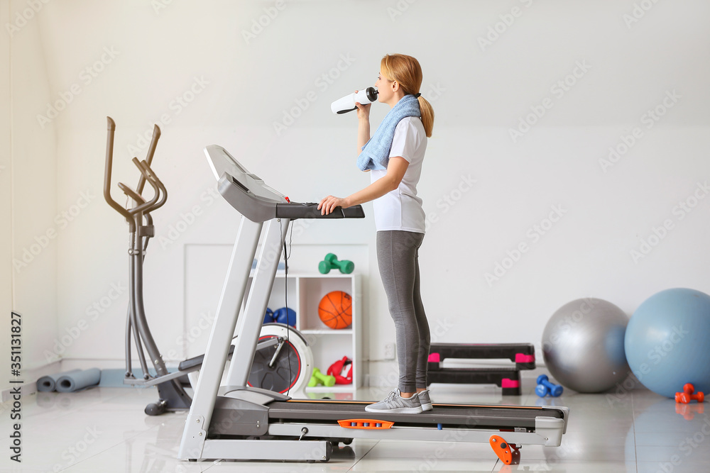 运动型女性在健身房跑步机上训练后喝水