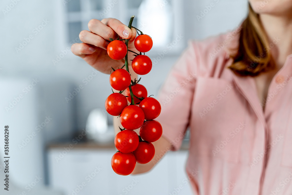 女人手里拿着成熟的樱桃番茄。厨房背景。裁剪的图片。健康的食物。