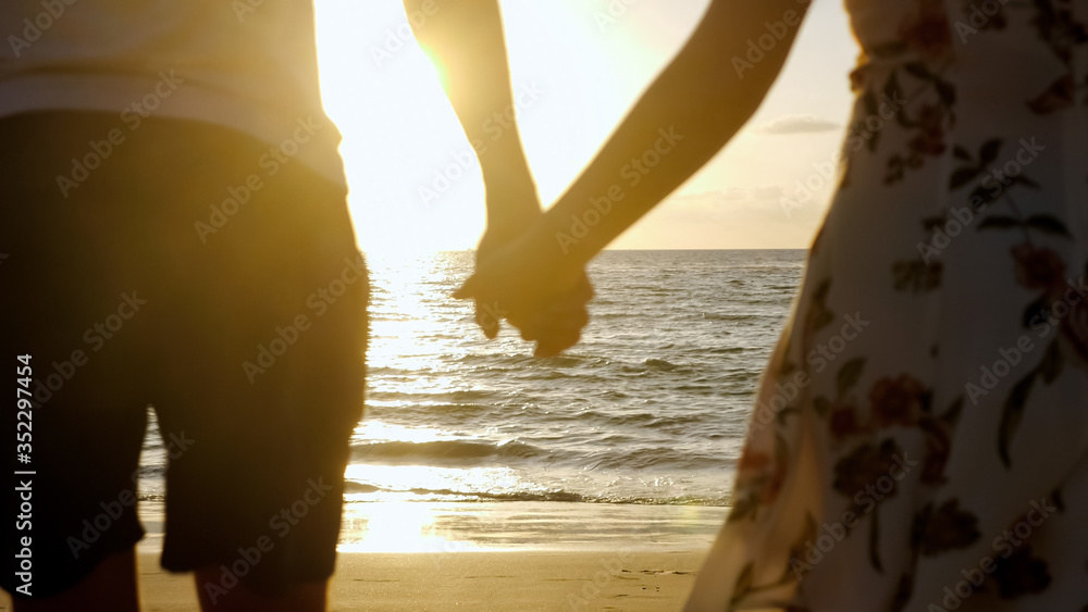 年轻的一家人在海滩上携手奔跑，在地平线上落日余晖下奔向无边无际的大海