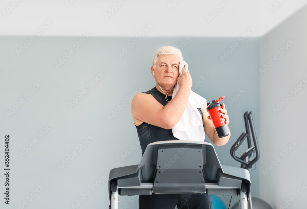 老年人在健身房跑步机上训练后喝水