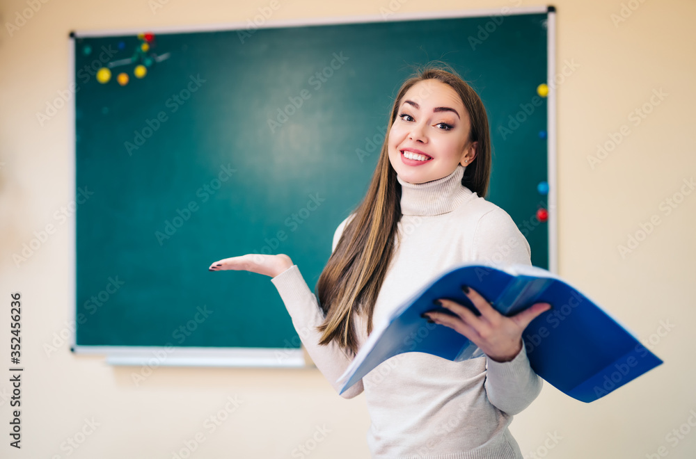 Young teacher is standing near blackboard in classroom. Showing I don`t know