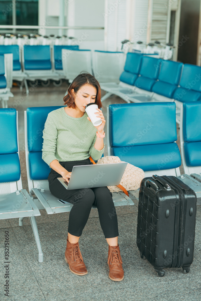 年轻的女商人坐在机场时使用笔记本电脑并喝咖啡。